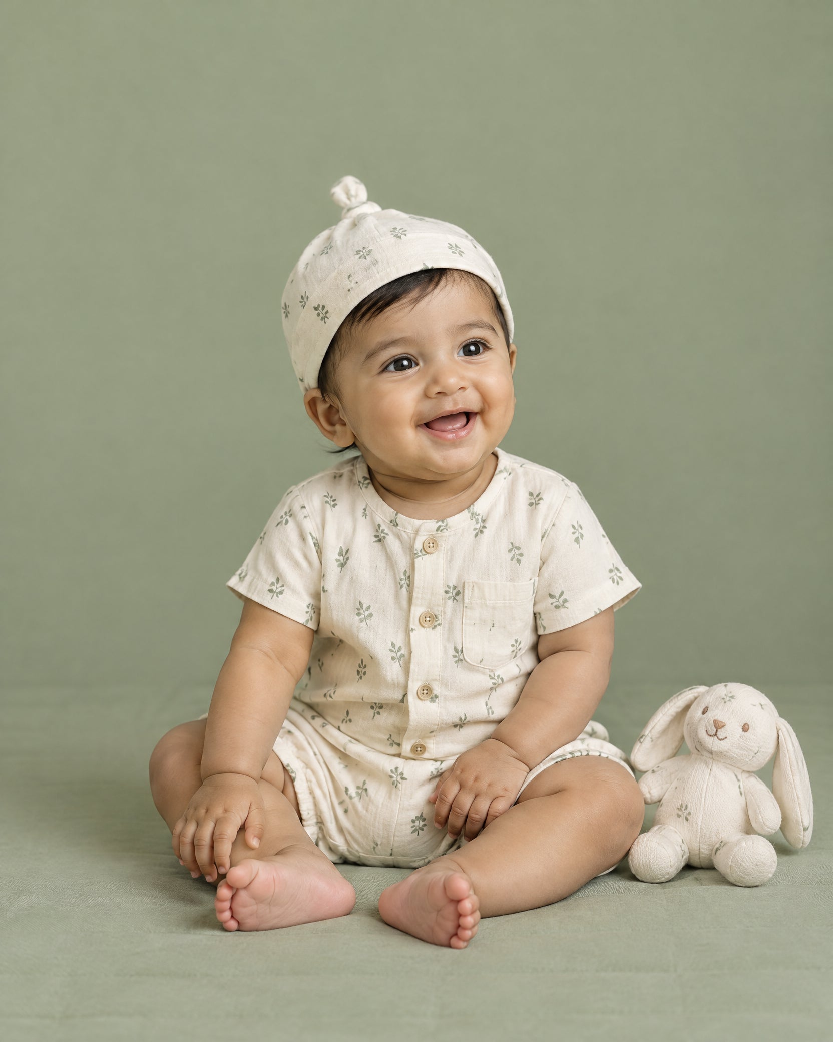A smiling baby wearing a soft cream romper against a sage background